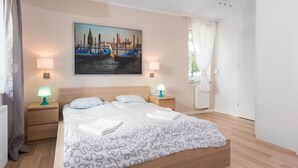 Ein ordentlich eingerichtetes Schlafzimmer mit einem Bett, zwei Nachttischen, einem Stadtbild und einem Fenster mit Vorhängen.