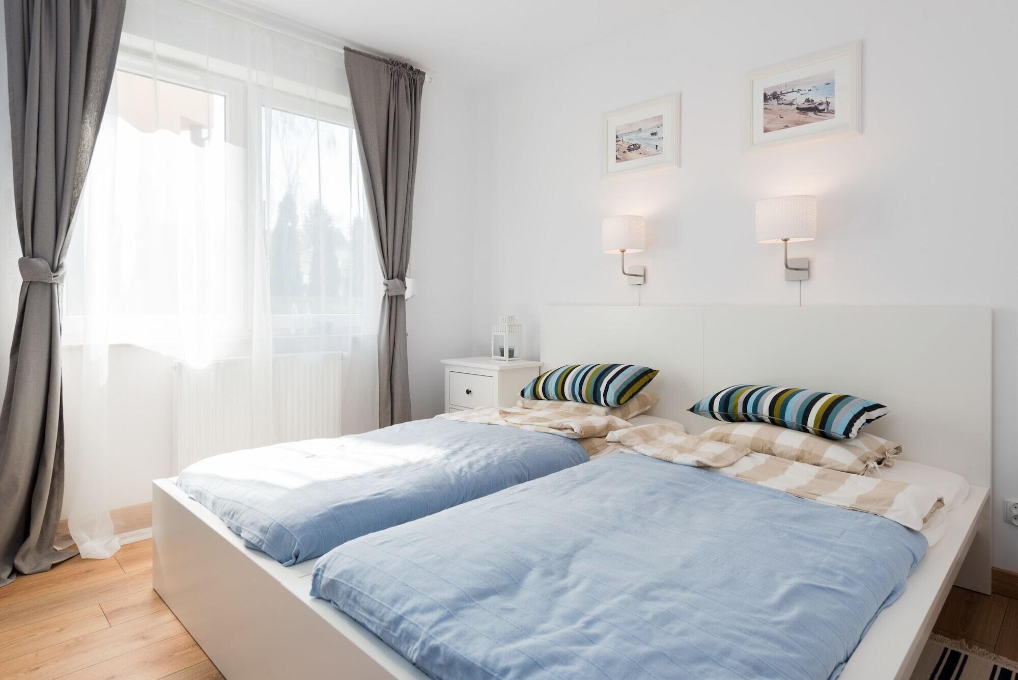 A bedroom with a bed, curtains, bedside tables, wall-mounted lamps, and two framed pictures.