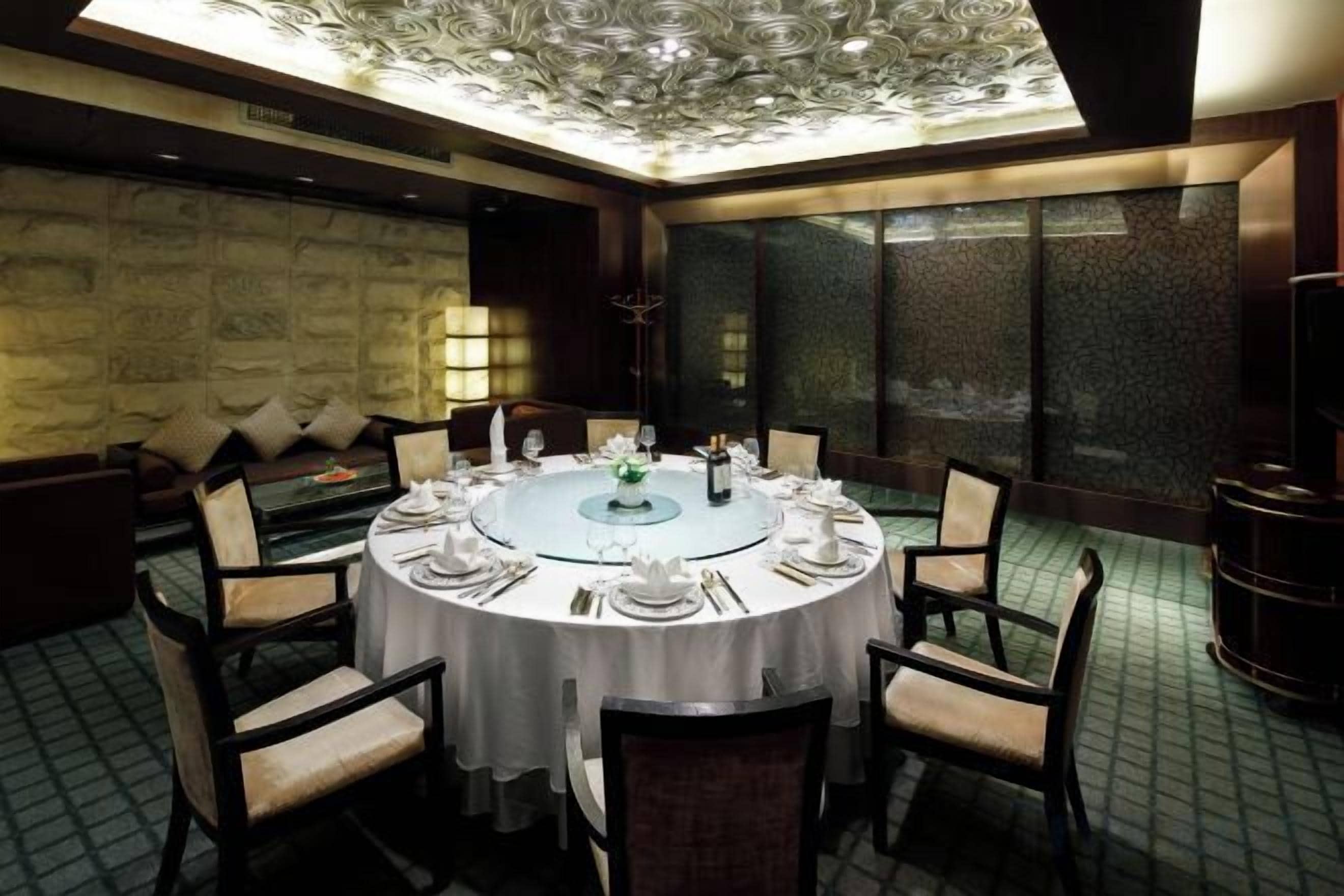 A round dining table with chairs, set for a meal, in a room with a patterned floor and a stone wall.