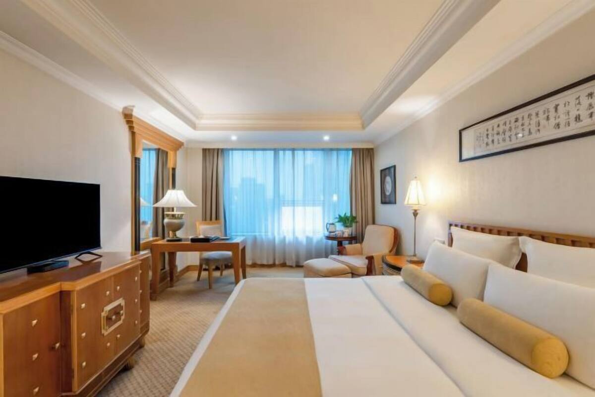 Habitación de hotel con una cama grande, televisión, escritorio con silla y una mesita de noche con lámpara.