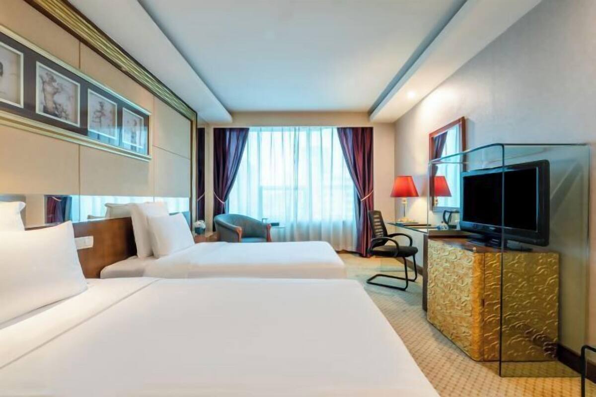 Una habitación de hotel con dos camas, televisión, escritorio con lámpara y ventana con cortinas.