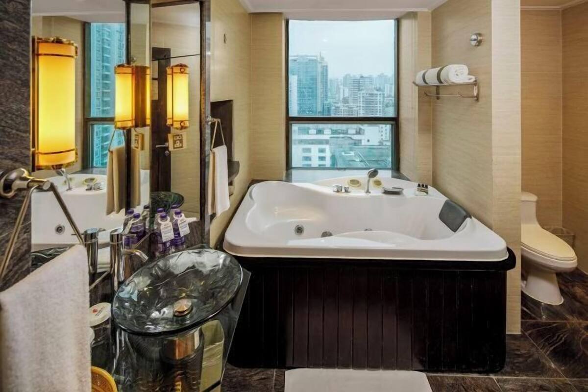 Un baño moderno con una bañera grande, un cubo de basura de vidrio y un inodoro.