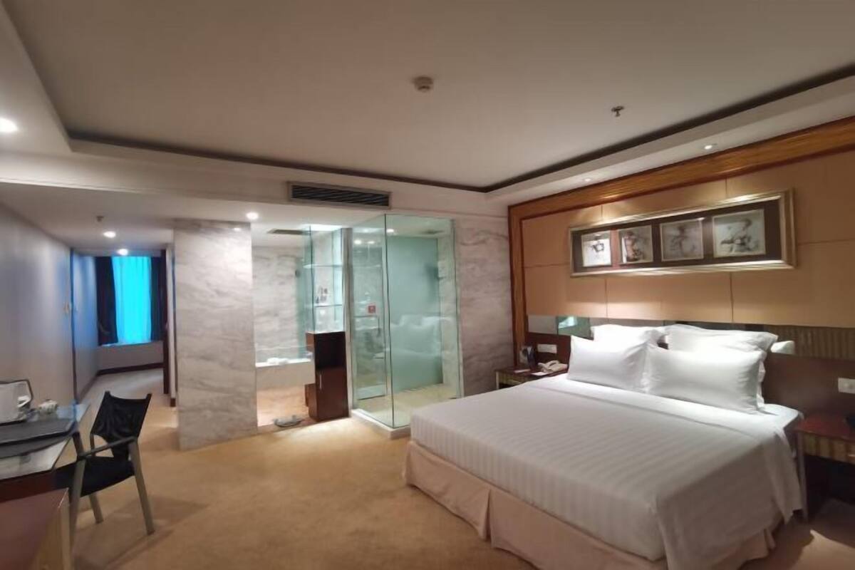 Habitación de hotel con una cama grande, un escritorio con silla, cabina de ducha de vidrio y cuadros en la pared.