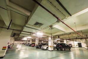 Un estacionamiento de varios niveles con varios coches aparcados, pilares de hormigón e iluminación elevada.