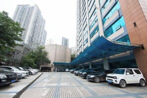 A parking area with multiple cars, a building with a blue awning, and tall residential buildings in the background. - Chongqing Air China Hotel (Guanyin Bridge Branch) (Chongqing)