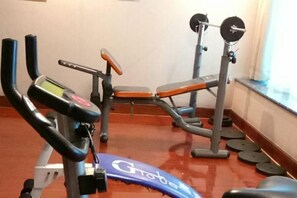 Ein Fitnessraum mit Trainingsgeräten, darunter ein Laufband, eine Bank und ein Kraftgerät.