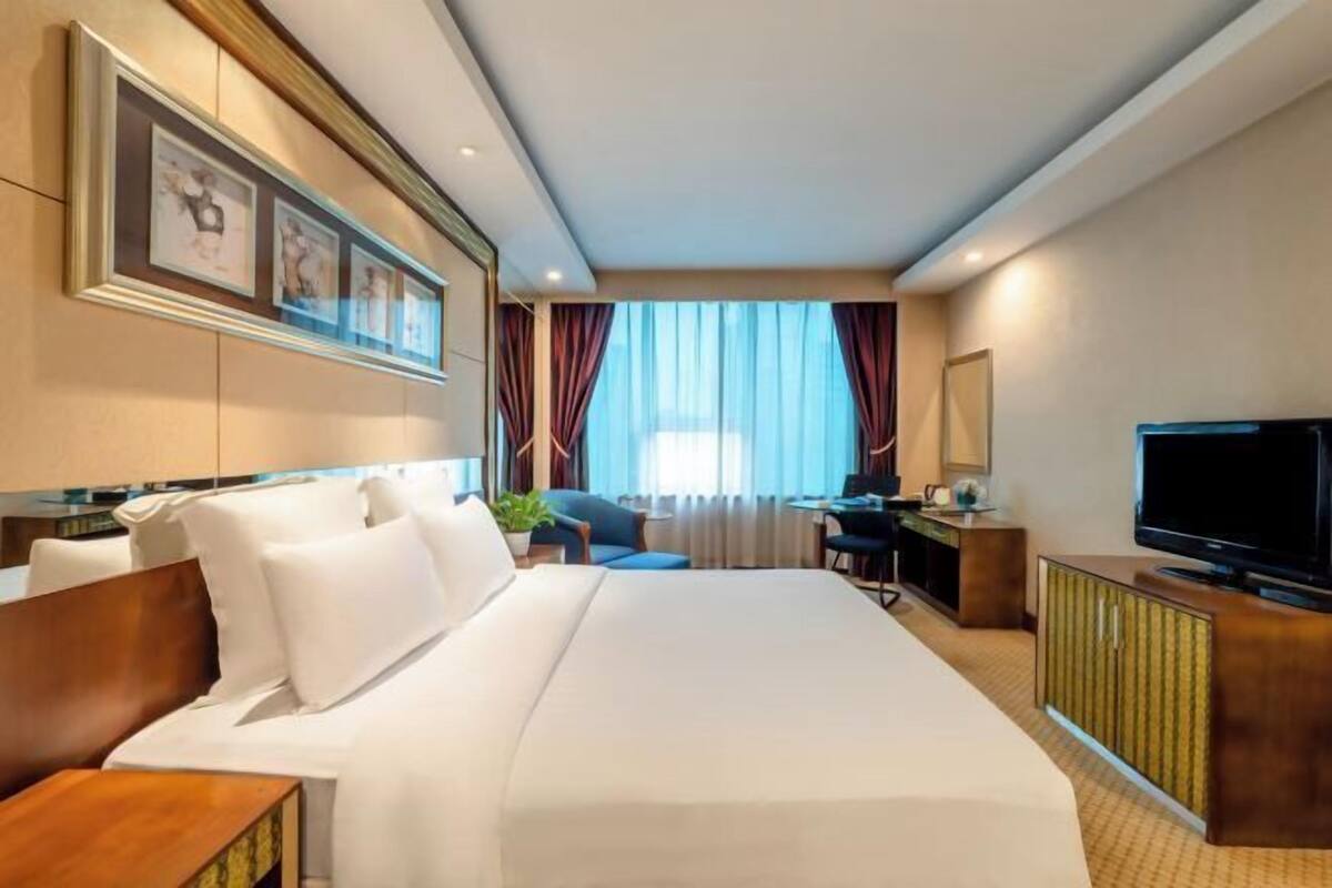 Habitación de hotel con una cama grande, un escritorio, una silla, un televisor y una ventana con cortinas.