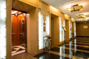 Un hall d’hôtel doté d’un ascenseur en verre, d’un comptoir de réception et d’un guichet d’enregistrement.