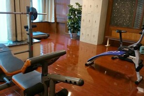 Un gimnasio con equipo de ejercicio, una banca y un estante fijado a la pared.