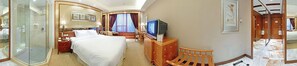 Ein Hotelzimmer mit Bett, Fernseher, Schreibtisch und einer Duschkabine.