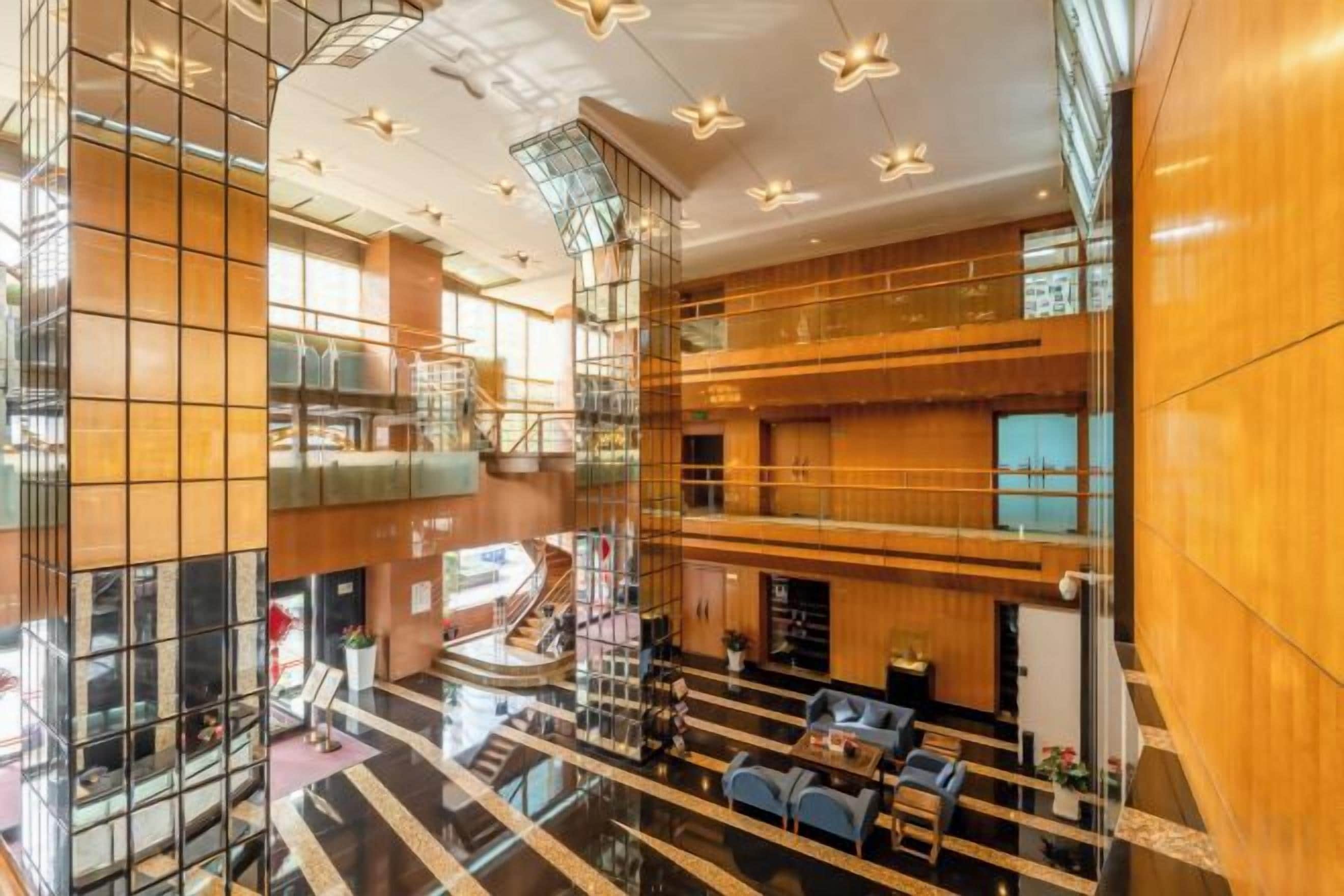 A spacious lobby with a central staircase, multiple seating areas, and a high ceiling with modern lighting fixtures.