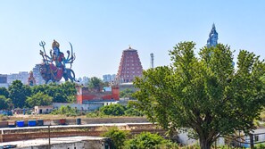 A large statue of a deity on a horse, a temple with a spire, and a tree in the foreground.