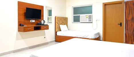 Una habitación de hotel con una cama, un televisor montado en la pared, un escritorio pequeño con un hervidor de agua y un equipo de aire acondicionado.