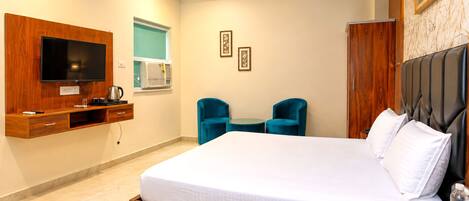 A hotel room with a large bed, a television mounted on a wooden panel, a small table with two chairs, and a wardrobe.
