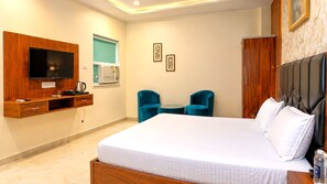 A hotel room with a large bed, a television mounted on a wooden panel, a small table with two chairs, and a wardrobe. - The Ora Hotel (Vrindavan)
