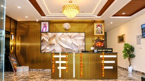 A reception desk with a large screen, a chandelier, and a potted plant. - The Ora Hotel (Vrindavan)