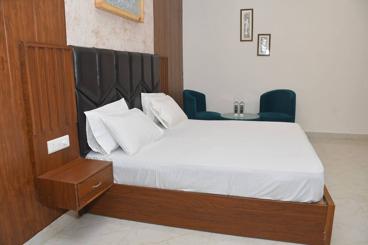 Un dormitorio con estructura de cama de madera, ropa de cama blanca, cabecera, mesita de noche y dos sillas color turquesa.