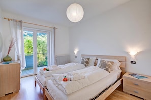 A bedroom with a double bed, bedside tables, a radiator, and a view of greenery through the window. - Agrilaura Apartments (Nago-Torbole)