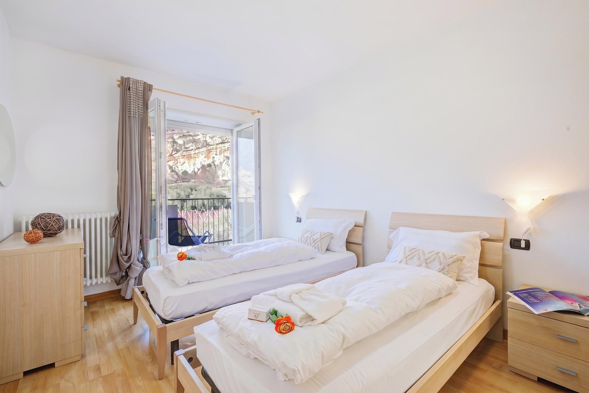 Ein Schlafzimmer mit zwei Betten, einem Nachttisch, einer Kommode, einem Heizkörper und einem Fenster mit Vorhängen.