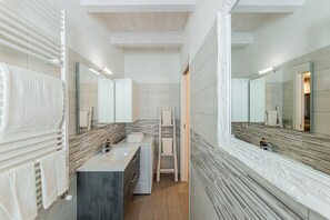 Une salle de bain moderne avec un grand miroir, un lavabo et un espace douche.