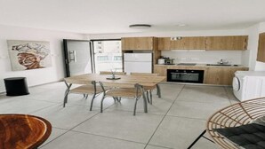 Une cuisine moderne avec des meubles de rangement en bois, une table à manger avec des chaises et une poubelle visible.