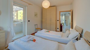 Un dormitorio con dos camas, un armario, una silla y una ventana con vistas a edificios.