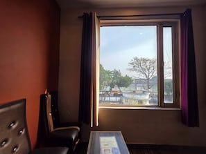 A room with a single black chair, a small table, and a window with curtains. - Hotel Ganges Park (Haridwar)