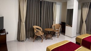 Une chambre d’hôtel avec un lit, une télévision, une petite table avec des chaises et un ventilateur de plafond.