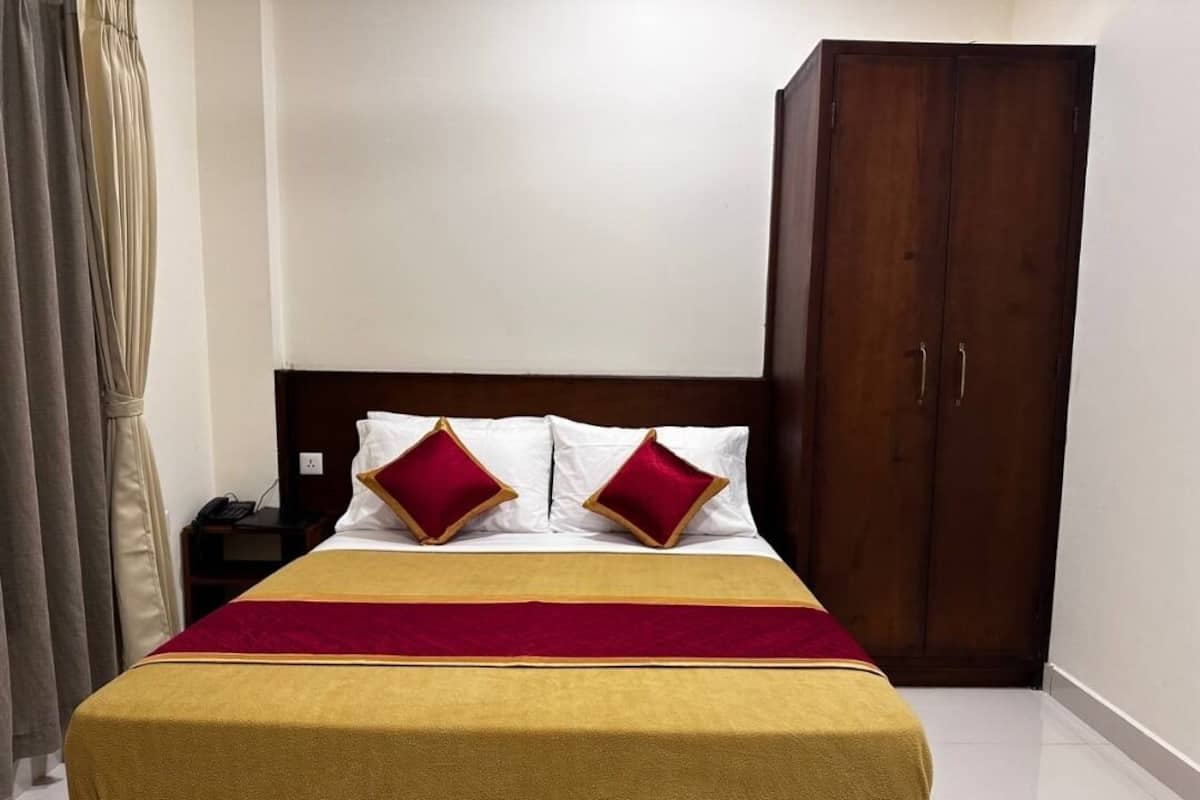 Una cama bien hecha con una colcha roja y amarilla, dos almohadas rojas y un cabecero de madera.