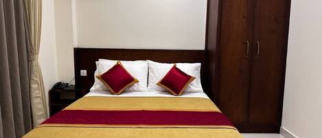 Una cama bien hecha con una colcha roja y amarilla, dos almohadas rojas y un cabecero de madera.