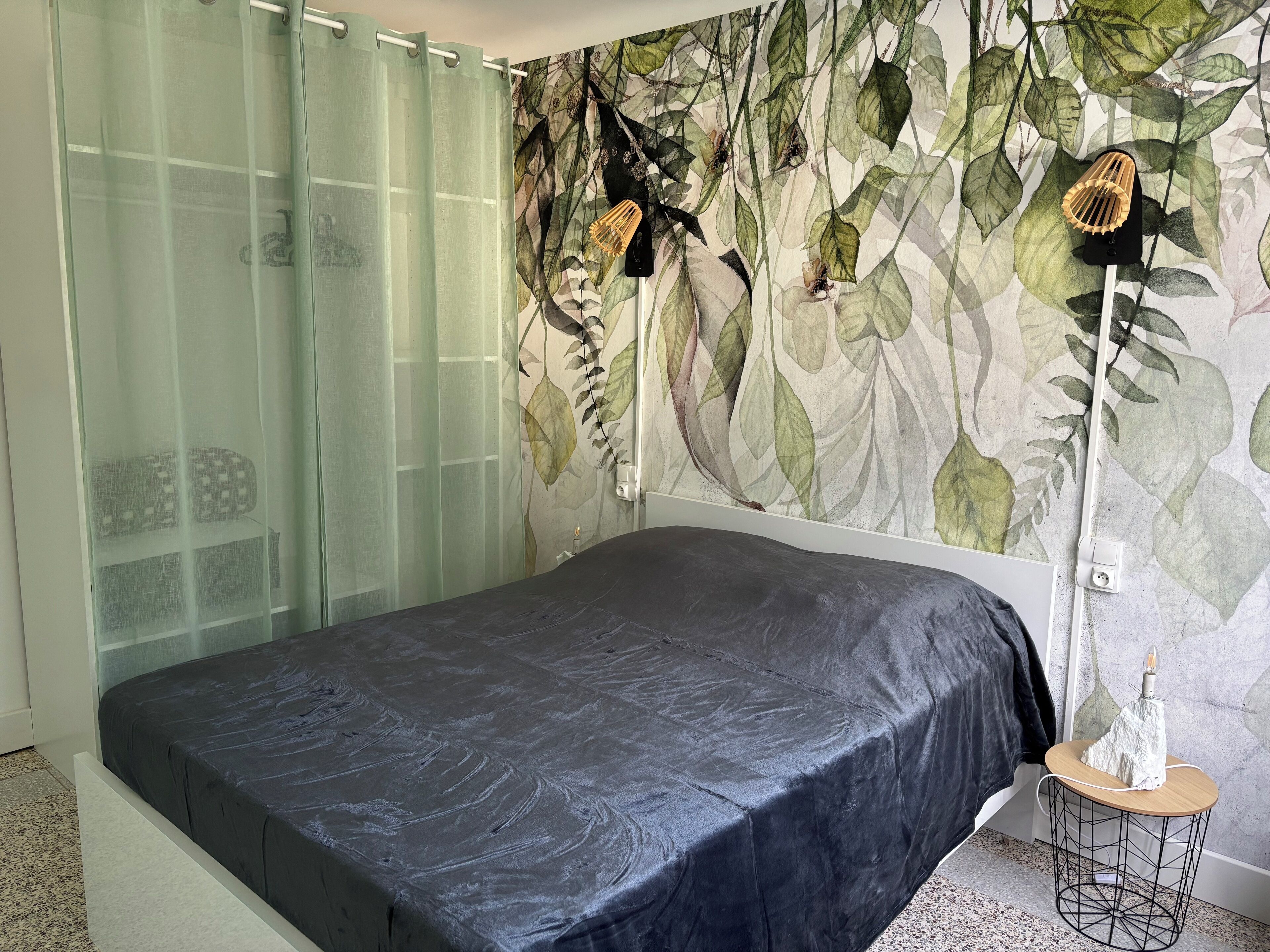 Un dormitorio con una cama, una lámpara de pared y una mesita.