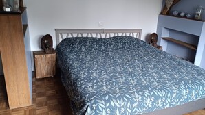 A bedroom with a bed, wooden nightstands, a dresser, and a shelf with decorative items.