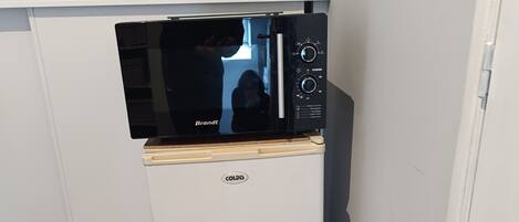 Una kitchenette compacta con un refrigerador blanco, un microondas negro y una encimera de madera.