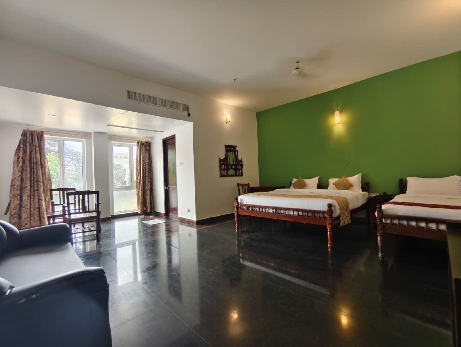 A hotel room with a large bed, a smaller bed, a desk, and a chair. There is a green wall and a window with curtains.