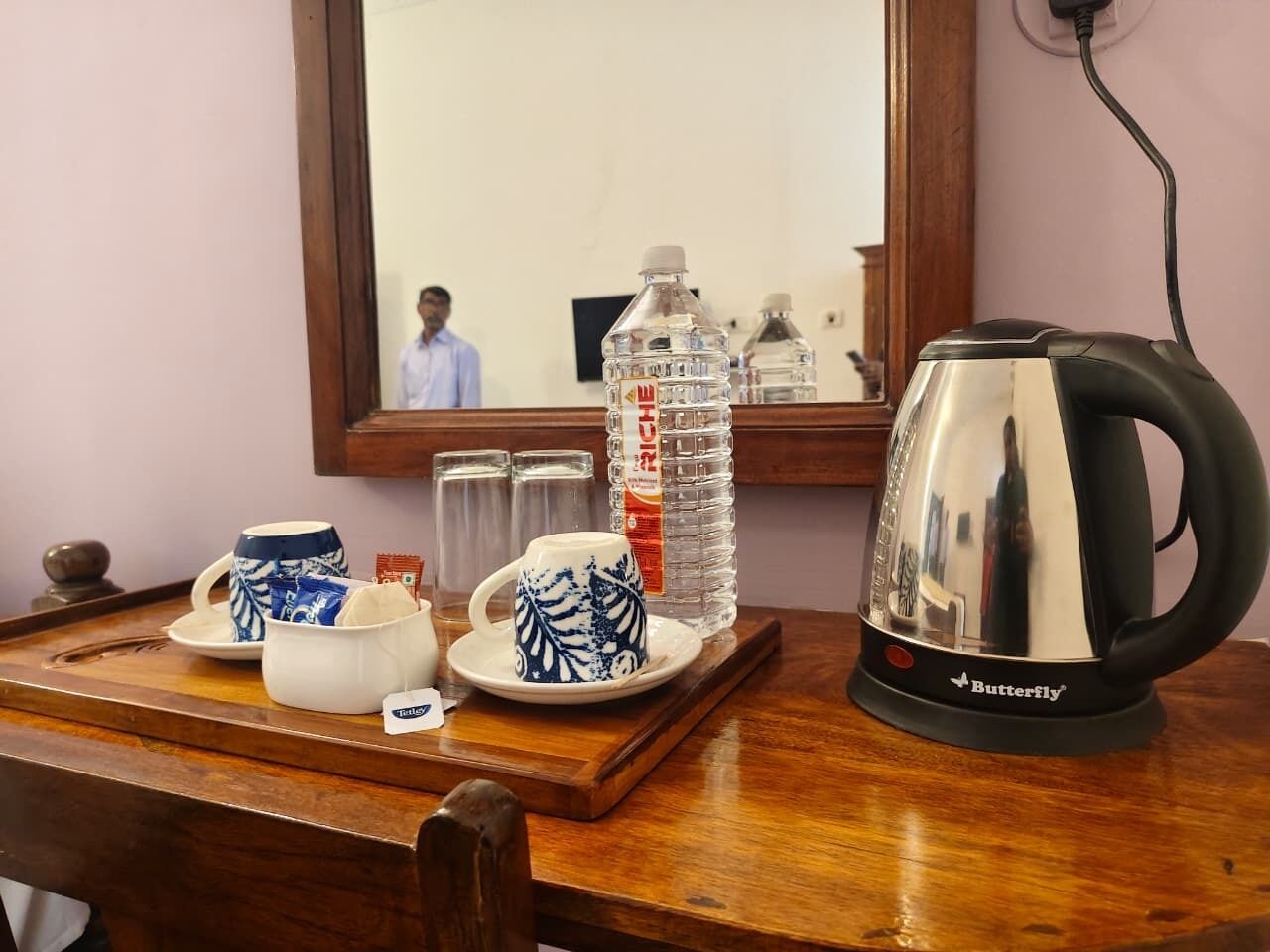 A wooden table with a tea kettle, two cups, a bottle of water, and a tray.