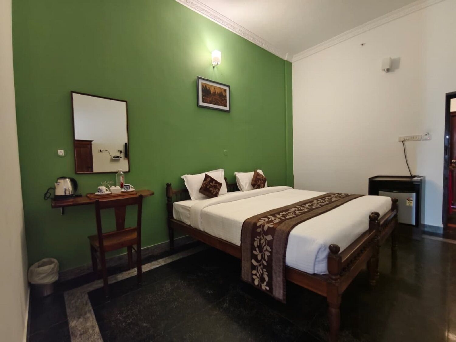 A hotel room with a bed, a desk, a chair, a mirror, and a picture on the wall.