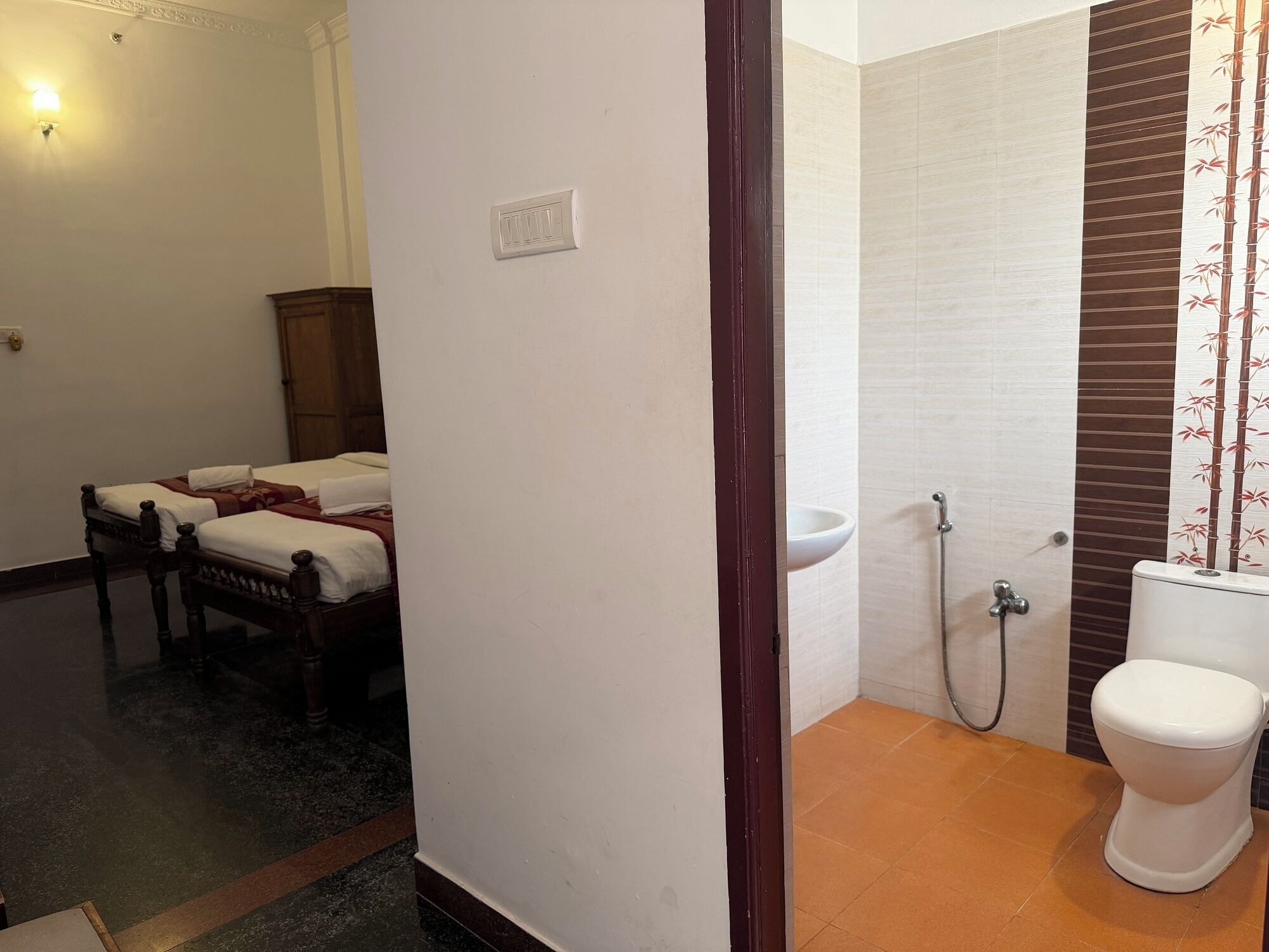 A bathroom with a toilet, sink, and shower. There are two beds in the adjacent room.