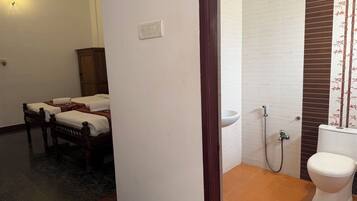 A bathroom with a toilet, sink, and shower. There are two beds in the adjacent room.