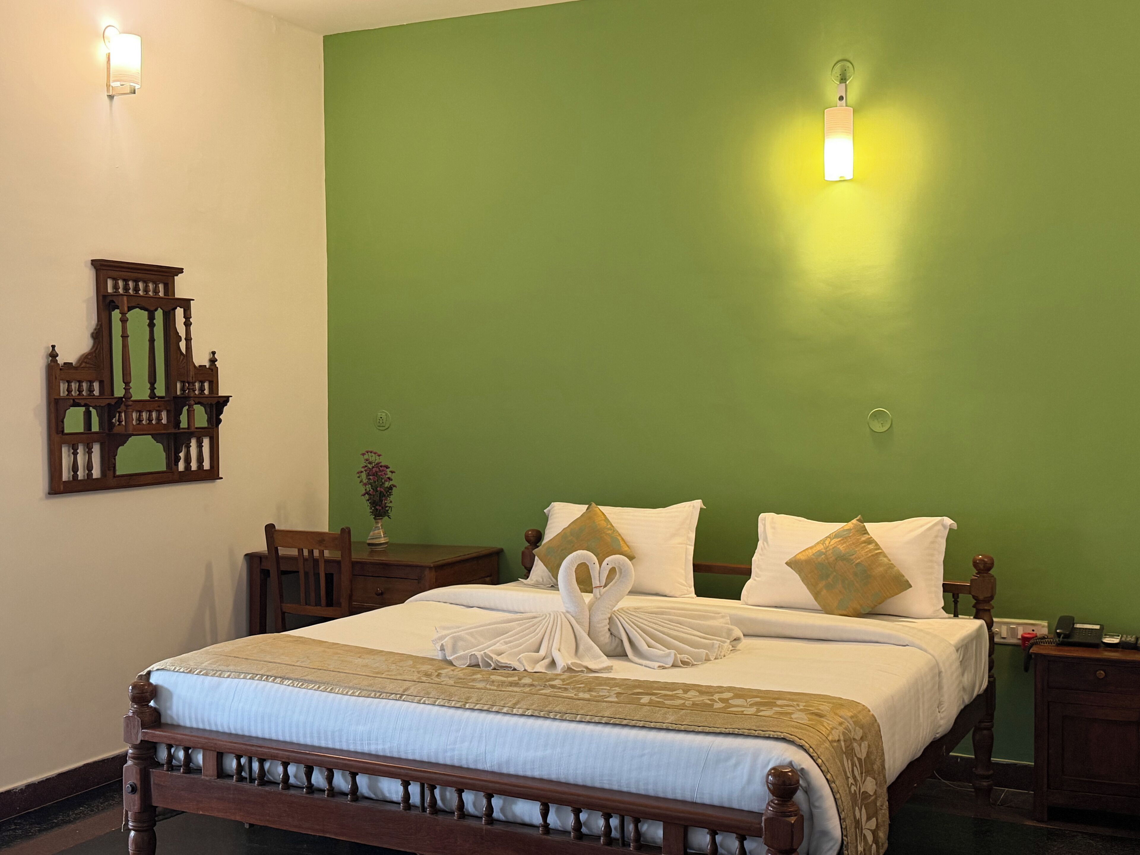 A neatly made bed with a decorative swan pillow arrangement, a wooden headboard, and a green wall.