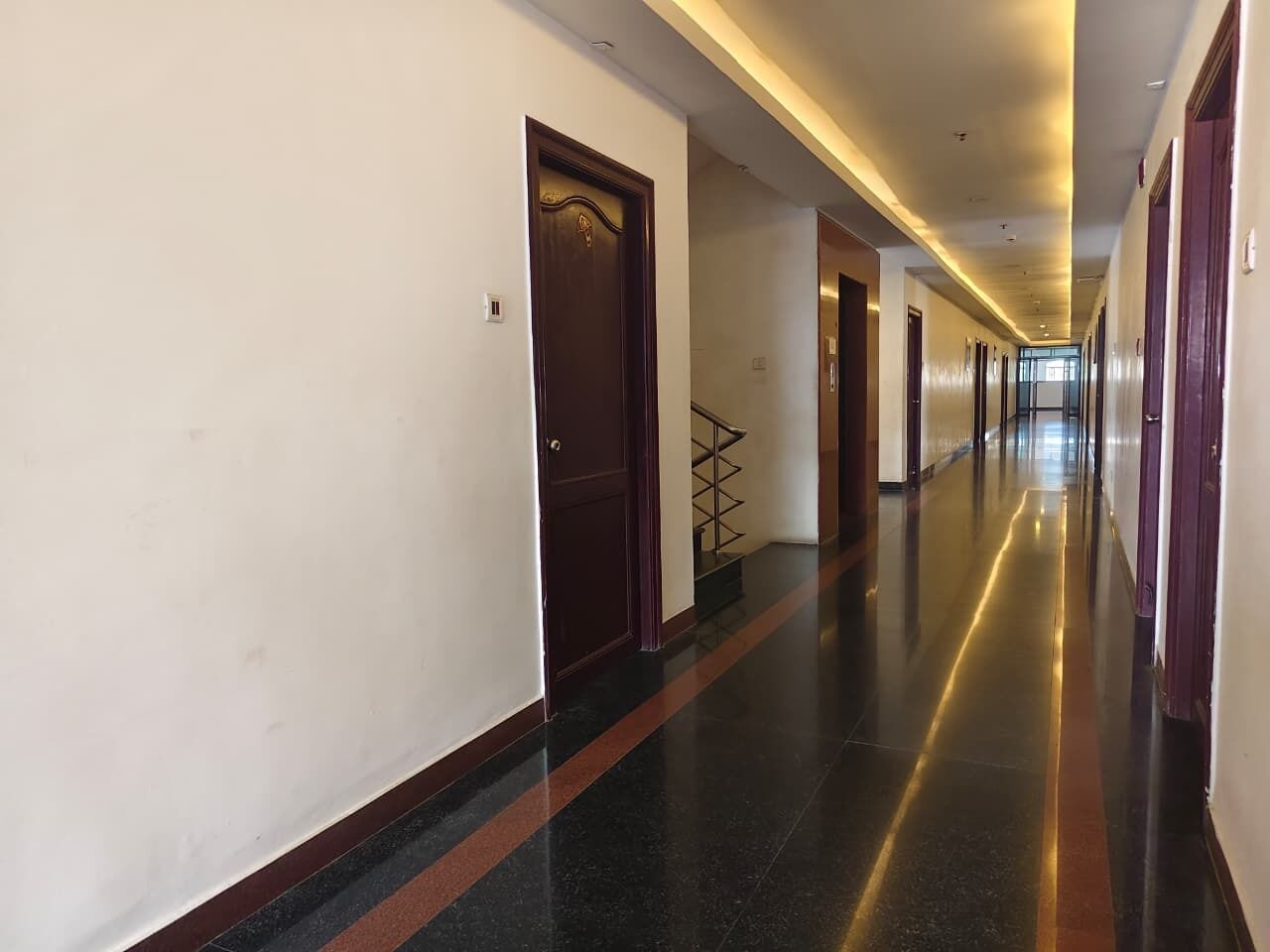 Un largo pasillo bien iluminado, con puertas a ambos lados, que conduce a varias habitaciones.