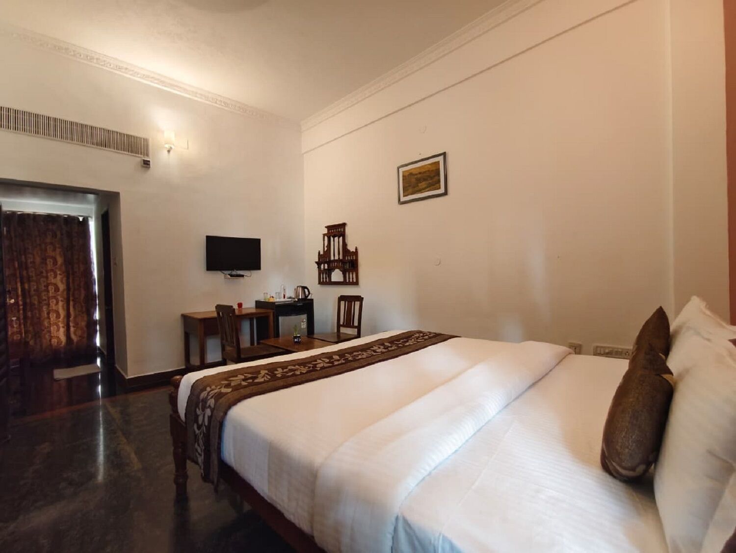 A hotel room with a bed, a desk with a chair, a television, and a picture on the wall.