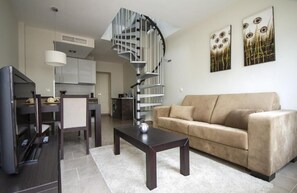 Una sala de estar moderna con un sofá, una mesa de centro y un televisor. Se ve una escalera de caracol que conduce a un nivel superior.
