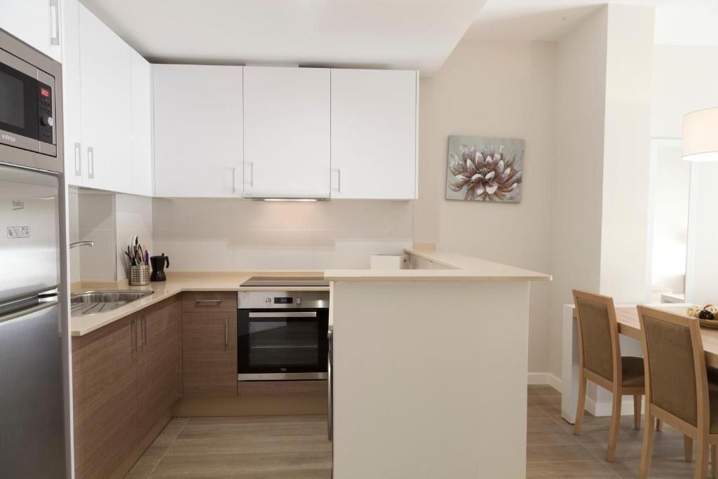 Una cocina moderna con armarios blancos, horno integrado y una pequeña isla con asientos.