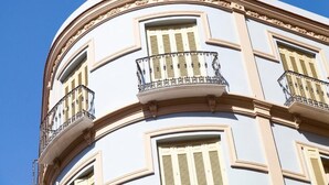 A corner of a building with a curved facade, featuring balconies with wrought iron railings and shutters. - Apartamentos Pinar Málaga Centro (Málaga)