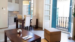 A modern living room with a dining area, a kitchen in the background, and a balcony with blue shutters. - Apartamentos Pinar Málaga Centro (Málaga)