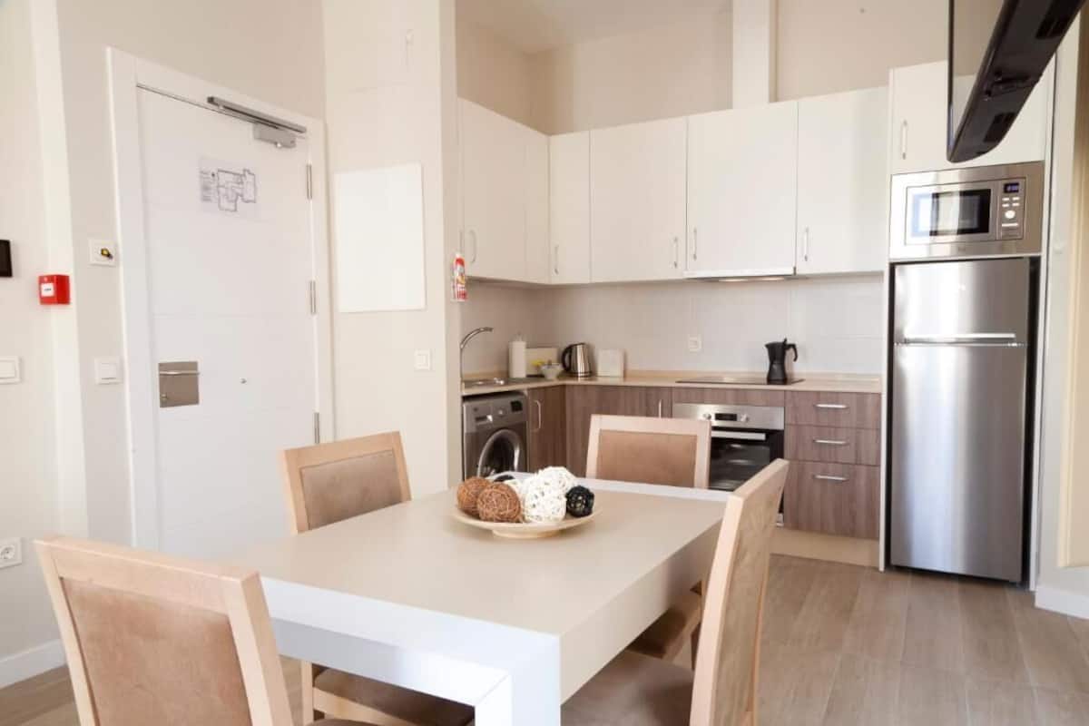 Une cuisine moderne avec des armoires blanches, des appareils en acier inoxydable et une table à manger avec des chaises.