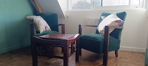 A room with two teal armchairs, a wooden table, and a sloped ceiling.