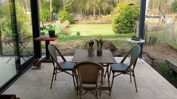 Un porche cubierto con una mesa y sillas, vista a un campo de golf y una valla de madera.