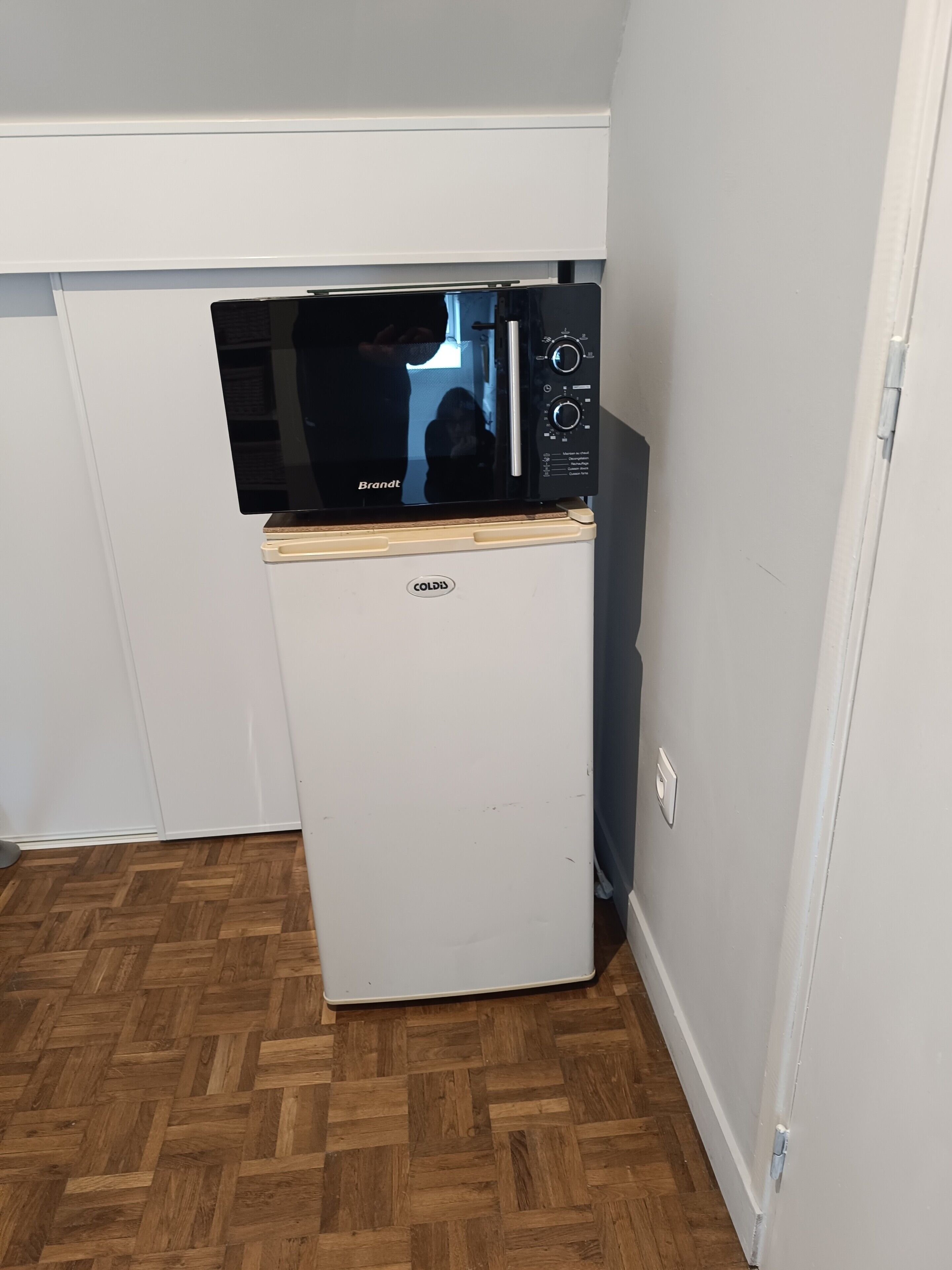 Una kitchenette compacta con un refrigerador blanco, un microondas negro y una encimera de madera.