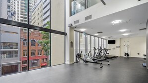 A gym with exercise equipment, large windows, and a view of buildings outside. - Bright 1-bed Retreat in Charlotte Towers (Brisbane)